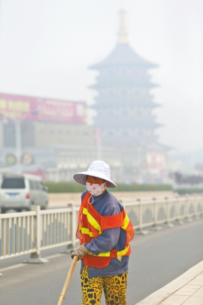 近日，在古都洛陽，環(huán)衛(wèi)工人身后的“天堂”被霧霾籠罩著。