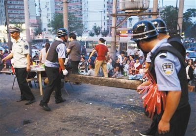 6月13日晚8點(diǎn)，朝陽路和青年路交叉口西側(cè)，一次聯(lián)合執(zhí)法行動(dòng)中，輔警與協(xié)管抬走商戶的燒烤用具。新京報(bào)記者 尹亞飛 攝