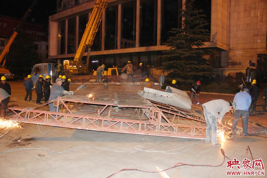 地面上的20多名工人對吊裝下的廣告牌進(jìn)行分割。