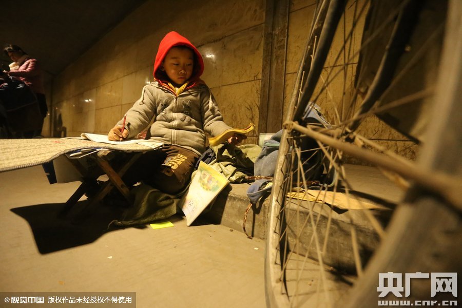 2015年11月8日晚，鄭州，7歲男孩涵洞橋下陪父母練攤，路邊燈下坐小馬扎上寫作業(yè)。