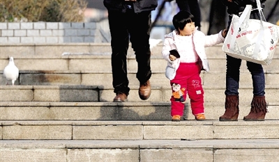 昨天中午，一女孩拉著家長(zhǎng)的手在紫荊山公園曬太陽(yáng)，氣溫升高，孩子的棉衣解開(kāi)了扣子。