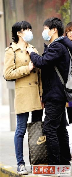 公交站臺上，一對年輕人戴著口罩，系緊衣領(lǐng)。